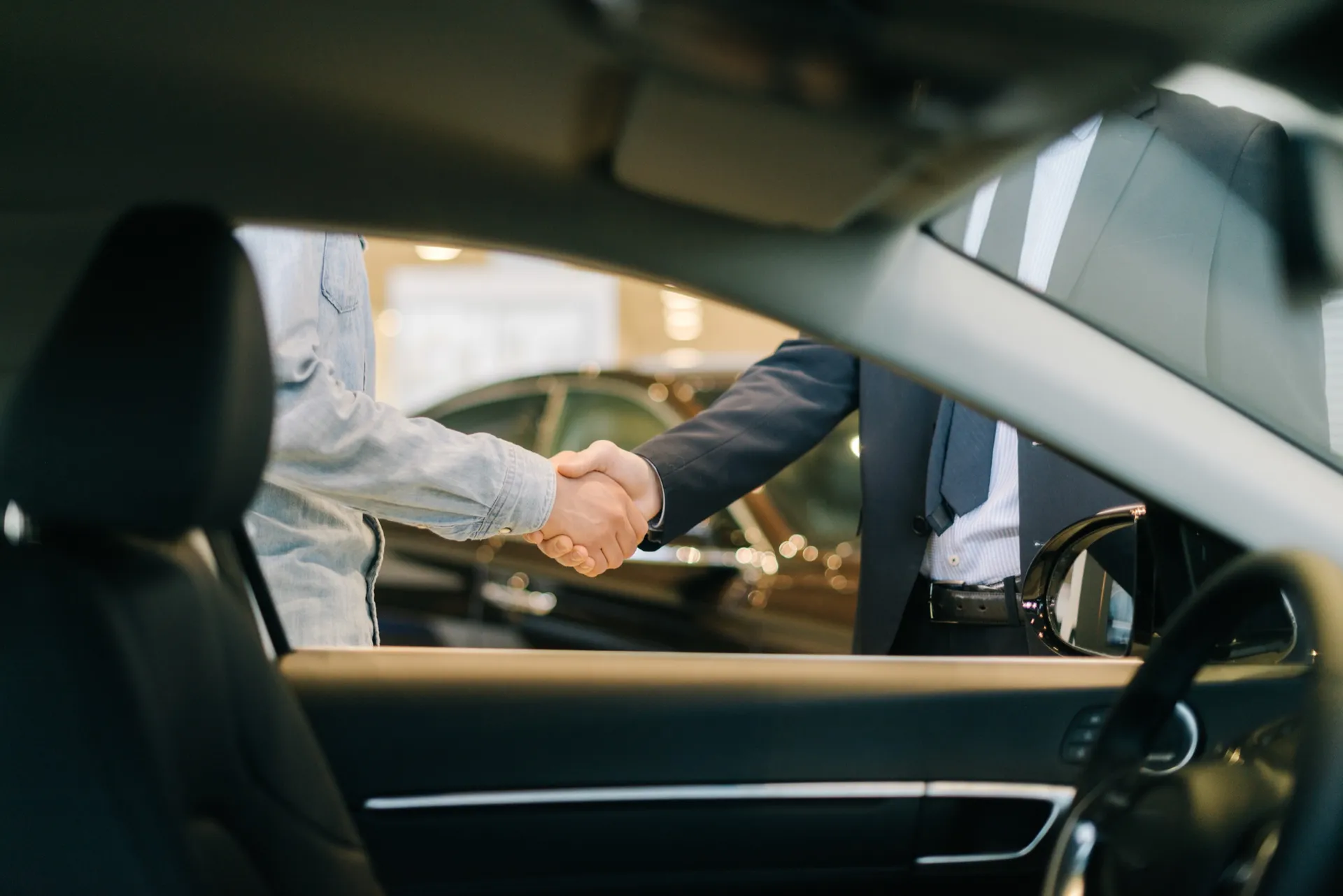 Two people shaking hands beside a car in a dealership showroom